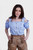 Woman wearing Lorelei Lederhosen, posing with hands in pockets, featuring detailed embroidery and a blue checkered blouse.