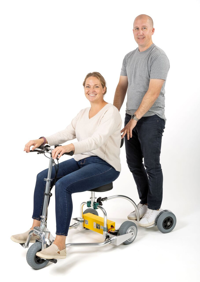 Man standing on the Standing Trailer hooked up to the TravelScoot Escape mobility scooter.