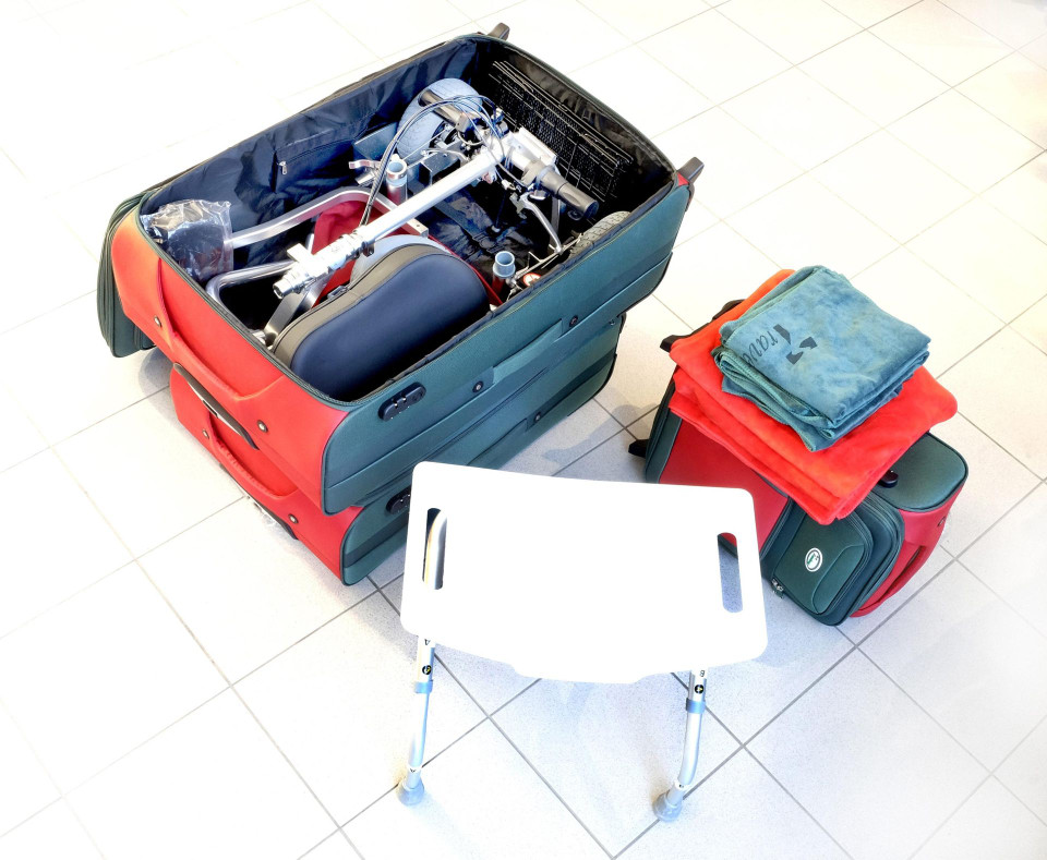 Main luggage with mobility scooter packed inside with towels and stool nearby.