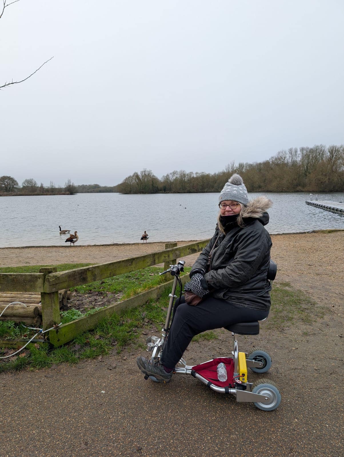 Woman sitting on travel scooter next to a lake.