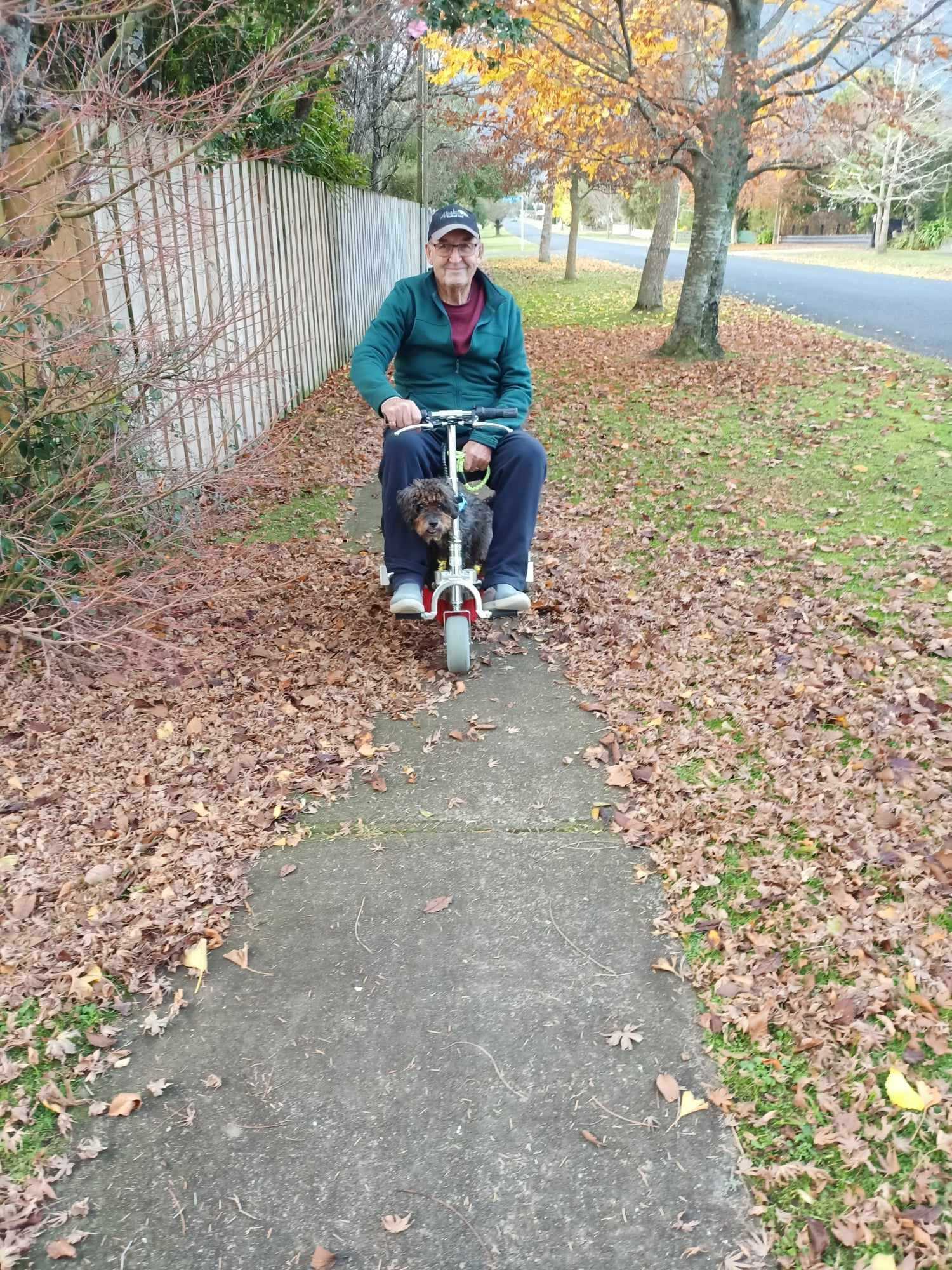 Man riding travel scooter on sidewalk in the Fall.