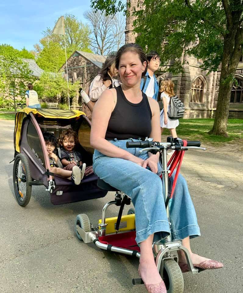 Mom towing a bicycle trailer with kids in it.