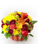 This stunning pumpkin is bursting with fresh, fragrant, fall blooms! Yellow and maroon mums, orange roses and lilies, with a touch of greens in a rustic orange pumpkin is a great way to enjoy the season.
