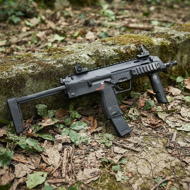 Side view of the Tokyo Marui MP7A1 Compact AEP Electric Airsoft SMG resting against a mossy stone wall in a forest.