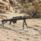 Galaxy G31 M82A1 Bolt Action Airsoft Sniper Rifle in Tactical Black set up on a bipod in a rocky outdoor terrain.