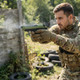 Player in camo firing the Raven R9 Replica M92 Gas Blowback Airsoft Pistol in Black & Green on an outdoor skirmish field