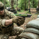 A player firing the Vorsk EU18 Gas Blowback Airsoft Pistol in Black with Green Top Slide over sandbag cover in a game.