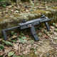 Side view of the Tokyo Marui MP7A1 Compact AEP Electric Airsoft SMG resting against a mossy stone wall in a forest.