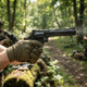 Action shot of the ASG R-357 Zastava Arms Gas Airsoft Revolver 4" in Black held by a gloved hand in a wooded field.
