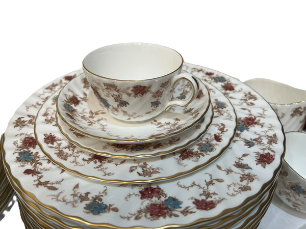 This is a place setting large collection of Minton "Ancestral" bone china dinnerware. The pattern features a rust and teal floral design with scalloped edges and gold trim.