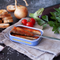 The image showcases an open tin of sardines served in a rich tomato sauce, placed on a dark, textured surface. The sardines are garnished or cooked with what looks like herbs, giving a fresh and homemade appeal to the dish. A fork rests inside the tin, suggesting that the sardines are ready to be enjoyed.

The scene is garnished with ingredients and elements that complement the main dish: there's a head of garlic and an onion with its papery skin partially peeled, both staples in flavoring many dishes. Fresh, ripe cherry tomatoes add a pop of color alongside an eggplant and some leafy parsley, hinting at the Mediterranean flavors that pair well with sardines. Crisp, golden croutons are scattered to the side, potentially for pairing with the sardines to add a satisfying crunch.

The overall composition is rustic and inviting, with the ingredients arranged in a casual yet deliberate manner. It suggests a simple yet flavorful meal, evoking images of a seaside meal in a Mediterranean setting. The colors are rich and warm, and the use of fresh produce implies the quality and taste of the sardines in the tin.