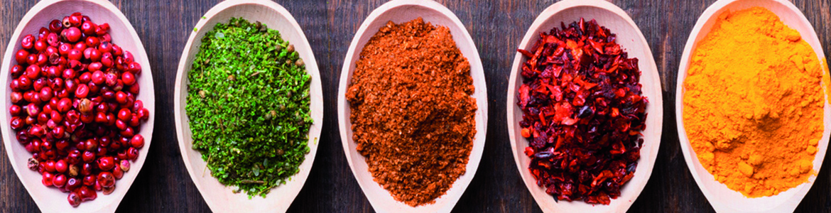 five wooden spoons filled with various peppers and spices