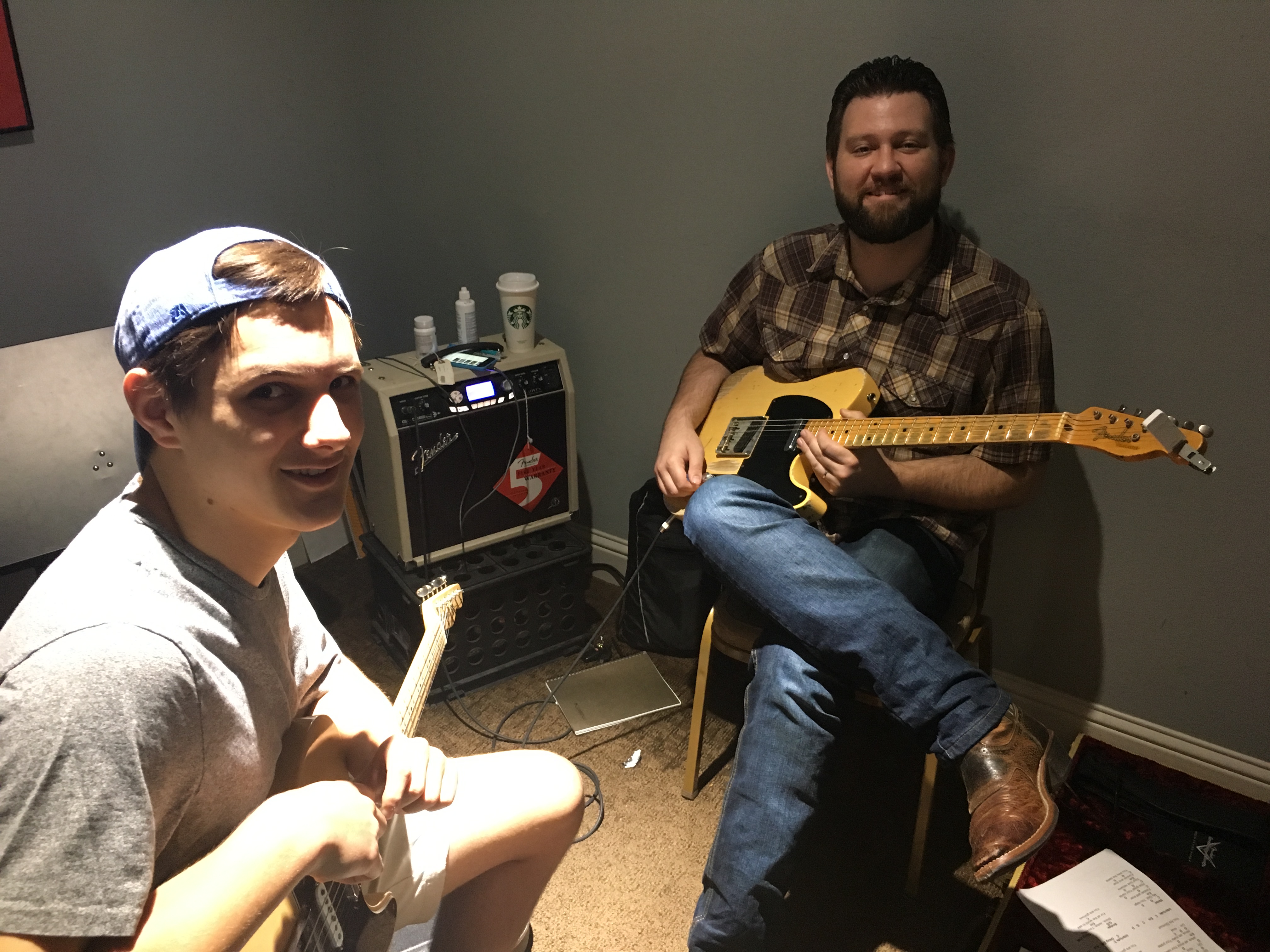 a man playing a guitar next to a man sitting on a chair