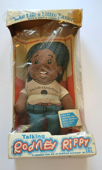 Talking Rodney Rippy Doll, vintage plush toy with a smiling face, curly hair, wearing a beige shirt with the quote "Take Life a Little Easier" and blue jeans, inside its original packaging.