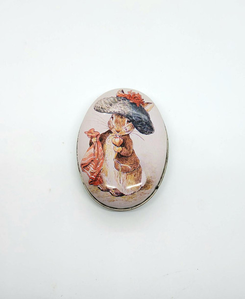 Schmid 1988 Schmid Beatrix Potter Rabbit Oval Tin, collectible vintage tin featuring an illustration of a rabbit wearing a large gray hat and a red scarf.