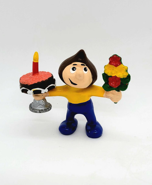 Hershey's 1984 Hershkins With Cake and Flowers PVC Toy Figure, colorful cartoon character holding a cake with a candle in one hand and a bouquet of flowers in the other.