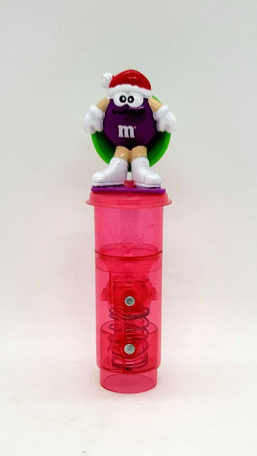 M&M's 2002 Minis Purple M&M Sledding Christmas Candy Topper, featuring a purple M&M character with a Santa hat and white gloves on a pink spring-loaded cup