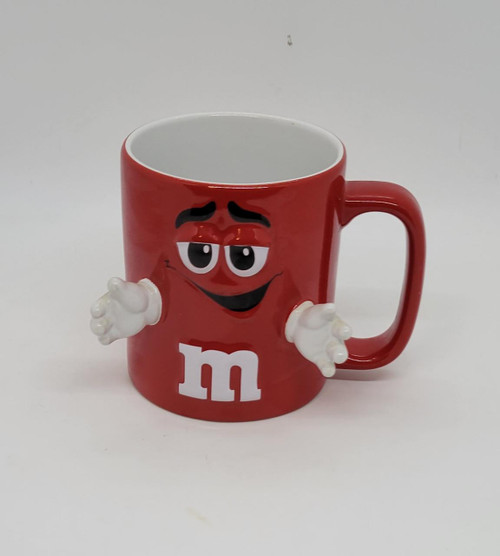 M&M's Red M&M With 3-D Hands Extended Coffee Mug, a red ceramic mug featuring a smiling M&M character with white 3-D arms and hands, and the white 'm' logo at the bottom.