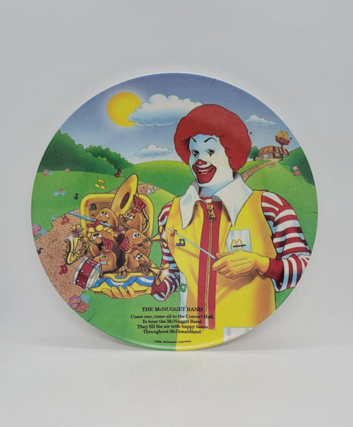 McDonald's 1989 The McNugget Band Melamine Plate, colorful circular plate featuring a clown conductor with band of anthropomorphic chicken nuggets playing instruments on a grassy landscape with a bright sun and clouds.