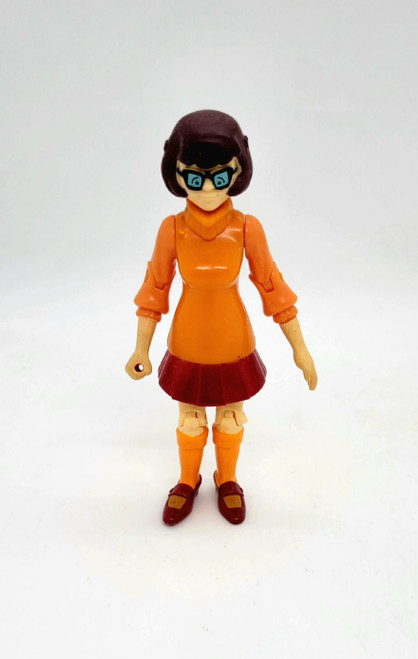 Velma 4 inch tall action from Scooby-Doo. Velma has her orange sweater and socks on.  She is wearing a brown skirt and shoes with her black glasses. 