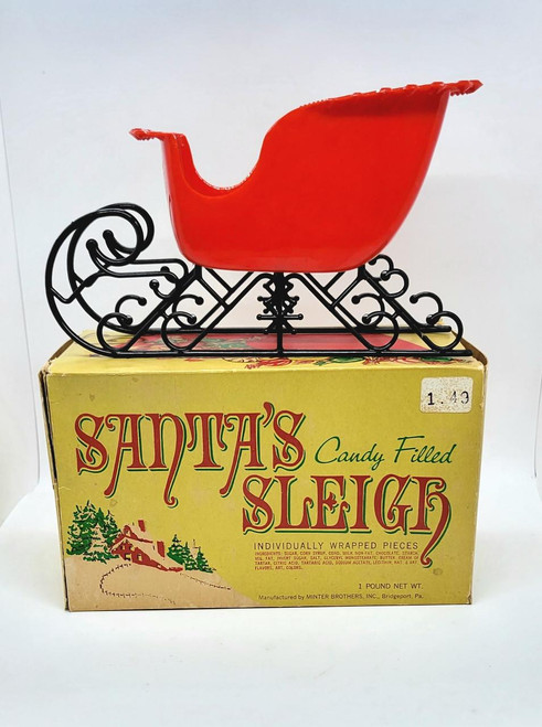 Minter Brothers Vintage Minter Brothers Plastic Candy Filled Santa's Sleigh, red candy-filled sleigh on black wire runners atop a yellow box with holiday design.
