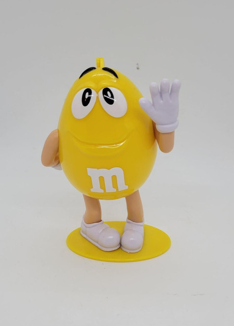 M&M's 2018 Yellow M&M Character Case Plastic Figure, yellow M&M character with arms, white gloves, white shoes, smiling face, and waving hand.