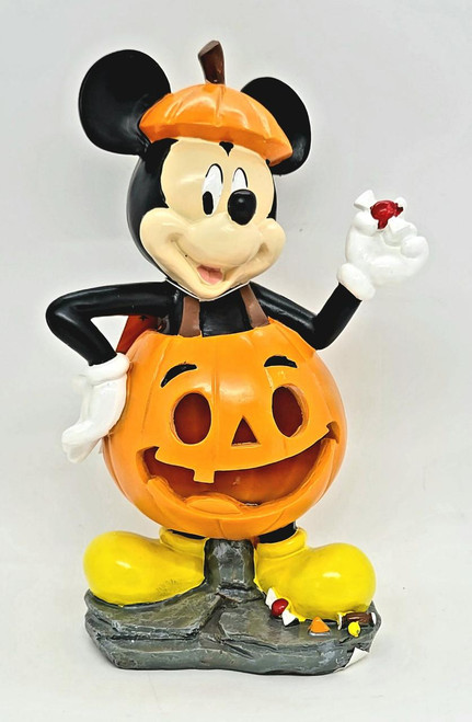 Disney's Mickey Mouse LED Light-up Halloween Garden Statue, Mickey Mouse dressed in a pumpkin costume with jack-o'-lantern face, wearing a pumpkin hat, yellow boots, holding a small candy, and standing on a textured base.