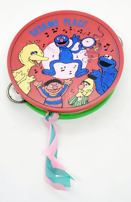 Product Sesame Street Vintage Kids Sesame Place / Sesame Street Red / Green Tambourine Souvenir, colorful tambourine featuring Sesame Street characters Elmo, Big Bird, and Oscar the Grouch with musical notes and ribbons.