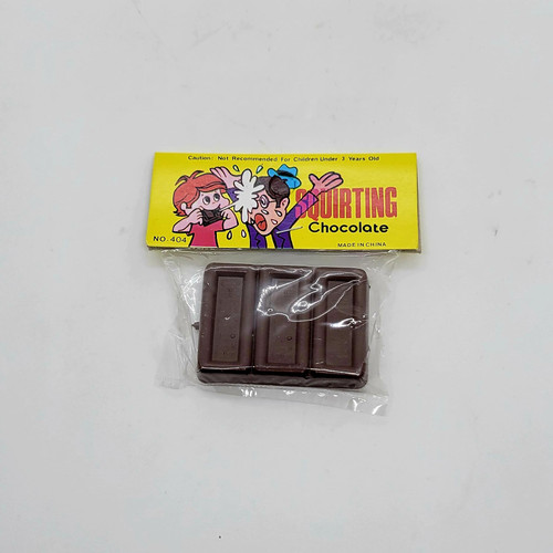Unbranded Squirting Chocolate Novelty Gag Toy, chocolate bars in clear plastic wrapping underneath a yellow packaging with cartoon characters, warning label about suitability for children under 3 years old.