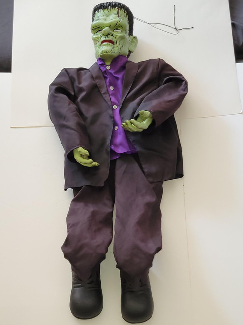 Gemmy 36 inch Frankenstein Hanging Halloween Decor, large green Frankenstein face with stitched scars, wearing a dark suit and purple shirt, with outstretched arms, for spooky Halloween decoration.