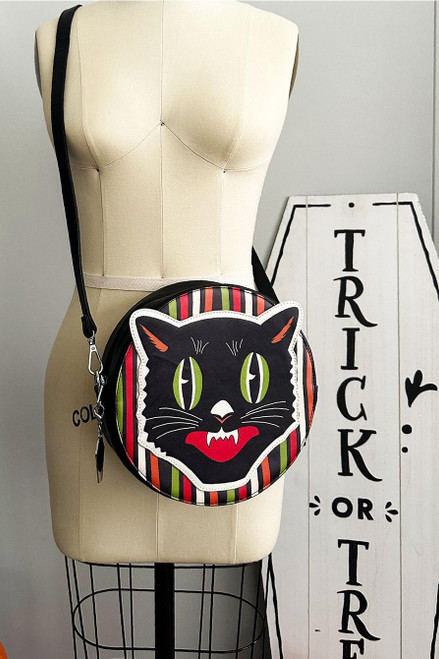 The Oblong Box Shop Haunted Holiday Cat Crossbody Purse, black cat face design with green eyes, red tongue, striped border in black, red, green, orange, and white, on a round black purse with adjustable strap.
