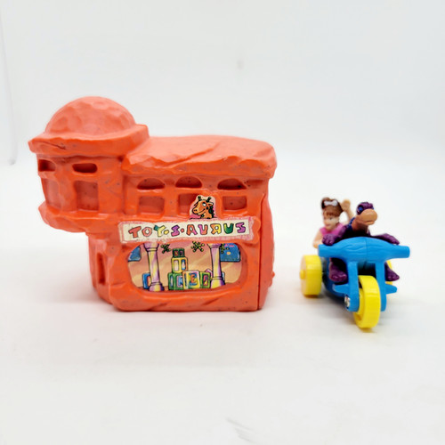 McDonald's Happy Meal toy of Pebbles and Dino riding on a blue tricycle with a orange Toy-S-Aurus from the 1994 The Flintstones series.  Toy-S-Aurus is based on the stone age version of Toys "R" Us.
