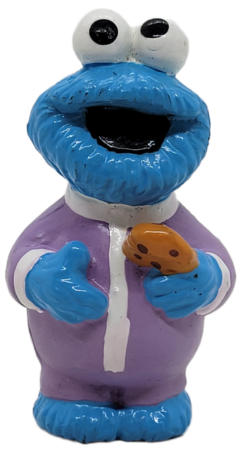 Sesame Street 2.5-inch tall PVC toy figure of Cookie Monster wearing purple pajamas with white trim.  Cookie Monster is holding his bedtime chocolate chip cookie in his left hand.