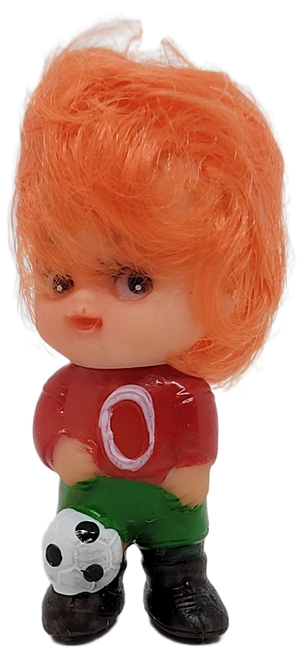 Vintage 2.5-inch tall rubber doll featuring a soccer player with orange hair.  The doll is wearing green pants and red jersey with the number "0" in yellow.  The soccer player has soccer ball at their foot.