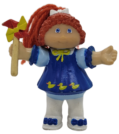 Cabbage Patch Kids 1985 figure of a red yarn hair girl wearing blue shirt with yellow ducks and white shoes and tights by OAA.  The girl is holding a pinwheel in her right hand. The figure stands 3-inches tall.