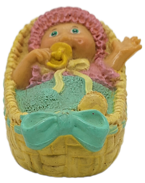 Cabbage Patch Kids 1985 figure of a preemie baby boy with blue cover with yellow pink hat and top by OAA.  The baby has left hand in the air. The figure is 2-inches long.