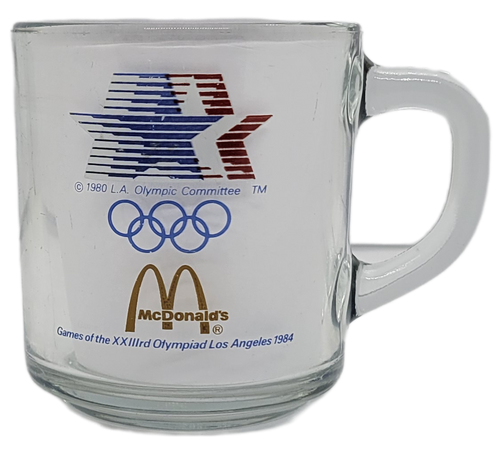 McDonald's 1984 Olympic Games clear glass coffee mug representing the water events of Sailing, Kayaking, Rowing & Swimming events. The mud has the Olympic Games logo, McDonald's logo & the 1984 Games red, white & blue stars on the opposite side. The mug stands 3.25-inches tall and 3" Wide without the handle.
