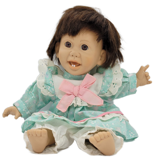 Gi-Go toys brunette girl doll with 2 teeth that measure 11-inches long. The doll has soft Polyester fiber body with rubber head, feet and hands. She is wearing light blue dress with white and pink spots. The dress has pink ribbon and white trim and a white pants under the dress.