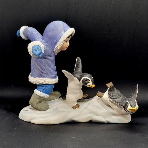 Watch Out figurine features an Eskimo boy chasing 2 penguins in front of him. The boy is wearing blue pants and purple jacket holding his arms out like the penguins. The figurine is a hand painted porcelain figurine crafted in Malaysia. Michelle Emblem's figurine is 8-inches wide by 6.5-inches tall and 4-inches deep.