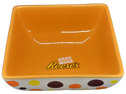 Reese's ceramic candy dish with "Need More Reese's" on the bottom of the inside of the orange bowl and a white outside with yellow, brown and orange polka dots. The candy dish is 5-inches by 5-inches and 2-inches tall.