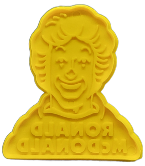 McDonald's 1980 yellow plastic cookie stamp featuring Ronald McDonald from the shoulders up. Ronald McDonald is a clown who is the primary mascot of the McDonald's all-American restaurant chain for over 50 years. The cookie stamp is 3.5-inches by 3.25-inches in size with a depth of 1/4-inch.