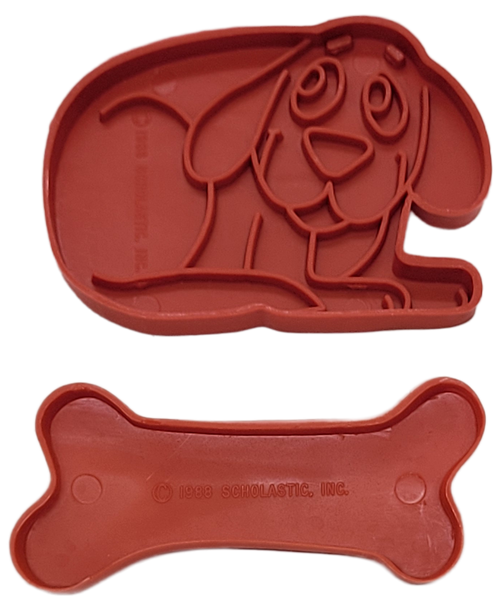 Scholastic 1988 red plastic cookie cutter set of Clifford the Big Red Dog and his bone. The Clifford cookie cutter is 3-inches long by 2-inches and the bone cutter is 3-inches long by 1.25-inches wide. Clifford, a 20-foot-tall red dog who loves stories, and his owner, Emily Elizabeth, enjoy new adventures as they explore their island home.
