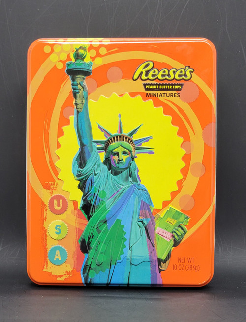 Reese's Peanut Butter Cups miniatures empty tin with Statue of Liberty and USA theme. The tin was produced in 2015 and is 8-inches long and 6.25-inch wide by 2-inches high. The bright colored tin would have contained Reese's Peanut Butter Cups miniatures.