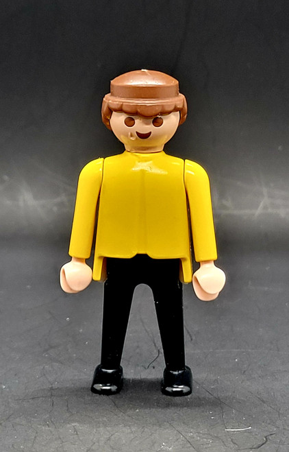 Geobra the German manufacture of Playmobil 1974 Male with brown hair 3-inch tall figure for ages 4+. The figure is wearing a yellow shirt and black pants and shoes. The figure is missing his hat and accessories.