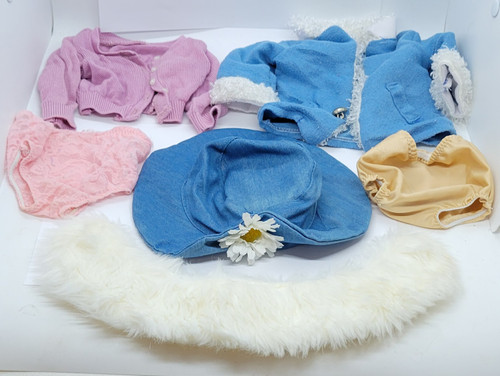 Collection of doll clothing accessories, including a blue denim hat with a white daisy, a pink cardigan, a blue jacket with faux-fur trim, undergarments, and a white faux-fur collar. The collection is for 18-inch dolls.