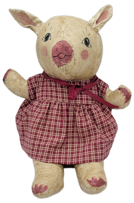 This approximately 9-inch-tall seated pig is made from sewn canvas and features the rustic, handcrafted appearance characteristic of primitive folk-art figures. The pig has a natural canvas-colored body with hand-painted facial features, including expressive black eyes, rosy cheeks, and a reddish-pink snout.