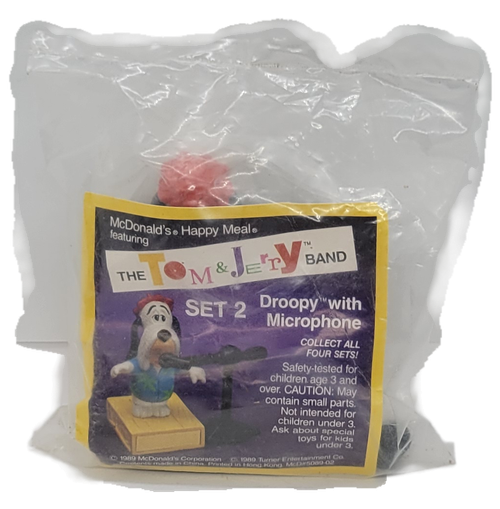 McDonald's Happy Meal toy of Droopy from the 1990 Tom and Jerry Band series of toys. Droopy is wearing a blue shirt with green leaves and is standing on a platform. The series of toys from the Tom & Jerry Band was available September 2-October 4, 1990.