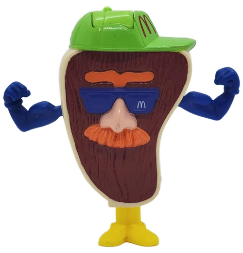 1993 McDonald’s Happy Meal Food FUNdamentals Slugger the Steak Toy, vintage anthropomorphic steak figure wearing a green McDonald’s cap and blue sunglasses, flexing blue arms on a yellow stand against a white background.