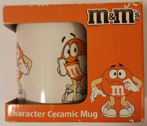 M&M Orange M&M's Character Ceramic Mug In Box, featuring an animated orange M&M character with a surprised expression, white gloves, sneakers, and the iconic M logo on the mug.