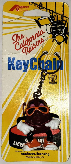 The California Raisins - Shades Keychain, featuring a cartoon raisin character with sunglasses, sneakers, and a cheerful pose, attached to a keyring on a yellow and white striped packaging.